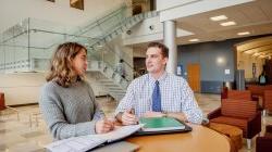 Two students sitting in the CELS building discussing things.